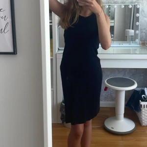 Svart ärmlös klänning H&M - Enkel svart klänning från H&M i ribbad bomull. Modellen är ärmlös med rund halsringning och rak passform som slutar strax ovanför knäna. Perfekt för en chill och stilren look.