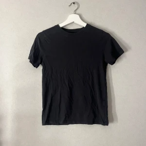 Svart basic t-shirt från H&M - En svart basic t-shirt från H&M med klassisk rund hals och korta ärmar. T-shirten är enkel och stilren, perfekt till jeans eller shorts. Tillverkad i mjuk bomull för en skön känsla hela dagen.