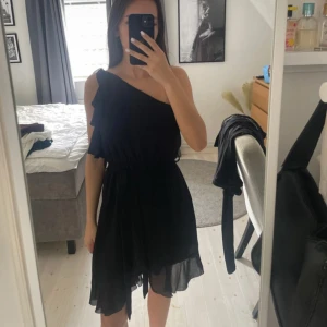 Svart oneshoulder kortklänning med volang - Sisters point storlek s. Svart klänning med volanger och knyte framtill, man kan ta bort snöret helt om man inte tycker om det. Klänningen är one shoulder. Bara använd några gånger. 
