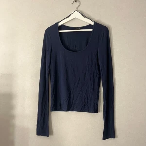 Mörkblå långärmad topp Gina Tricot - En basic mörkblå långärmad topp från Gina Tricot med rund, djup ringning. Tillverkad i mjuk bomullsmix som sitter skönt mot kroppen. Perfekt att styla med jeans eller kjol för en clean look. Har ett litet hål som jag lagat och it syns från långt håll.