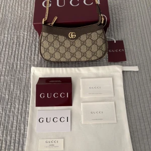 Gucci GG Supreme axelväska beige/brun - Säljer en snygg axelväska från Gucci i klassiskt GG Supreme-mönster. Väskan är beige med bruna detaljer, guldfärgad kedja och dragkedja. Materialet är canvas med skinninslag och väskan har en ikonisk GG-logga framtill. Perfekt storlek för det viktigaste.