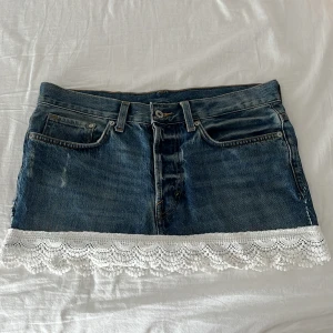 Low waist jeanskjol med spetskant  - Superfin kort jeanskjol från &Denim i klassisk blå denim med snygg vit spetskant nertill. Kjolen har fem fickor, knappgylf och bälteshällor. Kontakta mig gärna vid frågor eller funderingar😊                                                  Midjemått rakt över: 41cm                                       Längd: 28cm