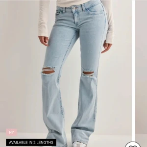 Ljusblå bootcut jeans med slitningar - Säljer ett par ljusblå bootcut jeans med slitna detaljer över knäna och råa kanter nertill. Jeansen har broderade bakfickor med röd och vit vågig detalj. Klassisk femficksmodell i mjuk denim, perfekt för en avslappnad look.