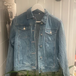 Klassisk blå jeansjacka - Säljer en klassisk blå jeansjacka med silverfärgade knappar och två bröstfickor. Har inga tecken på användning och är i en bra kvalite. 