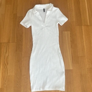 Vit ribbad kortklänning H&M Divided XS - Supersnygg vit ribbad kortklänning från H&M Divided i storlek XS. Klänningen har krage, v-ringning och korta ärmar. Den är figurnära och stretchig, perfekt för en fräsch och enkel look. Materialet är mjukt och bekvämt bomullsmix.