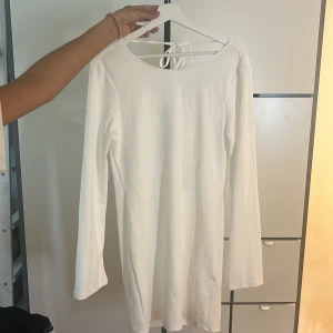 Vit långärmad klänning med öppen rygg - Säljer en stilren vit långärmad klänning med snygg öppen rygg och knytning i nacken. Klänningen har en figurnära passform och är perfekt för dig som gillar enkel men elegant stil.