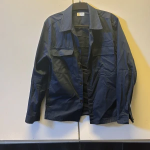 Mörkblå skjorta från Tiger of Sweden - Säljer en stilren mörkblå skjorta från Tiger of Sweden. Skjortan har klassisk krage, knäppning framtill och en bröstficka med lock. Perfekt för dig som gillar en enkel men snygg look. Overshirten är lite skrynklig då den har varit bland andra kläder men är i mycket bra skick. Nypris på denna är runt 1999 -2499, mitt pris 449! Pris går att diskuteras! Hör av er vid minsta lilla fundering🤗