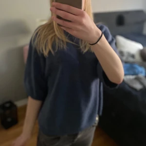 Blå stickad tröja med halvkort ärm - Mysig blå stickad tröja med halvkort ärm och avslappnad passform. Perfekt för lager-på-lager och enkel att styla till jeans eller kjol. Tröjan har en rund halsringning och är i ett mjukt material.