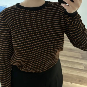 Randig tröja - Säljer en svart tröja med tunna orangea ränder i ett rutigt mönster. Tröjan har rund halsringning och långa ärmar. Aldrig använd.