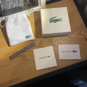 Silverfärgat armband från Lacoste - Snyggt armband i silverfärgad metall från Lacoste med diskret krokodillogga och mönstrad yta. Kommer med originalförpackning, tygpåse och certifikat. Perfekt accessoar för att lyfta din stil. Hör av er vid frågor💗 Pris kan diskuteras vid snabb affär!