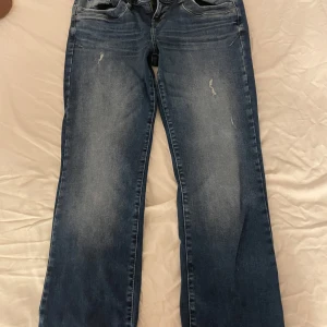 Blå bootcut jeans med låg midja - Säljer ett par klassiska blå jeans i bootcut-modell med låg midja. Jeansen har lätt slitna detaljer framtill och femficksdesign. Perfekta för dig som gillar en nice och avslappnad stil.