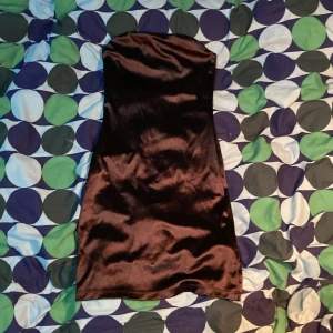 Mörkbrun axelbandslös mini-klänning - Säljer en mörkbrun axelbandslös mini-klänning i glansigt material. Klänningen har en tight passform och är perfekt för dig som vill ha en stilren och elegant look. Passar utmärkt till festliga tillfällen.
