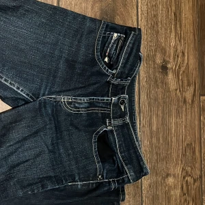 Mörkblå jeansbyxor med kontrastsömmar - Snygga mörkblå jeansbyxor med tydliga vita kontrastsömmar och klassisk femficksdesign. Byxorna har normal passform och stängs med dragkedja och knapp framtill. Perfekta till vardags för en stilren look.