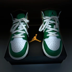Nike Air Jordans 1 MID (GS) Lucky Green/Black-White - Säljer ett par Air Jordans i kartong (i princip helt oanvända). Skorna har klassisk hög modell med vit tå och gröna paneler, vit- svart sula. 