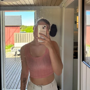 Rosa ribbad croppad linnetopp - Säljer en rosa croppad linnetopp med ribbad struktur. Toppen är ärmlös och har rundad halsringning. Perfekt för varma dagar och enkel att matcha med olika byxor eller kjolar.