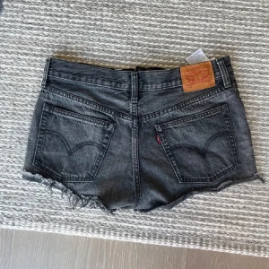 Svarta jeansshorts från Levi's 501 - Snygga svarta jeansshorts från Levi's 501 med råa fransar nertill och klassiska bakfickor. Shortsen är perfekta för sommaren. Ikonisk läderpatch baktill och slitna detaljer för en cool look.