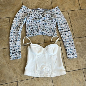 Blommig långärmad topp från ZARA och vit korsett-topp - Två snygga toppar! En blommig, smockad långärmad topp från ZARA i blå, vit och svart med offshoulder-modell. Till det en vit korsett-topp med smala axelband och markerade kupor. Perfekt att mixa och matcha! 100kr för båda