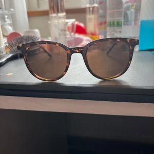 Bruna solglasögon från Gina Tricot - Snygga solglasögon från Gina Tricot med klassisk rundad form och brunmelerat skalmönster. Glasen är mörka och bågarna har en leopardlook. Perfekta för att lyfta din stil med en accessoar. Inga repor. Köpta för några år sedan men aldrig använda!