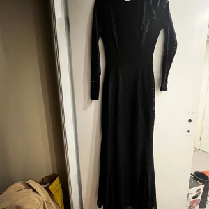 Svart långklänning med lång ärm - Säljer en elegant svart långklänning med lång ärm och figurnära passform. Klänningen har rund halsringning och är tillverkad i ett glansigt material som ger en lyxig känsla. Perfekt för dig som vill sticka ut på festen.