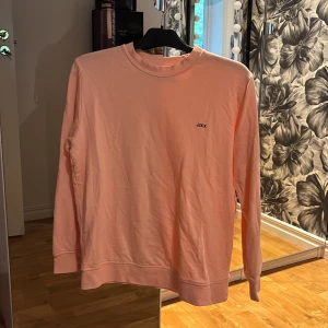 Ljusrosa sweatshirt från JJXX - Säljer en ljusrosa sweatshirt från JJXX med rund halsringning och diskret logga på bröstet. Tröjan har långa ärmar och är tillverkad i mjuk bomull, perfekt för en avslappnad stil.