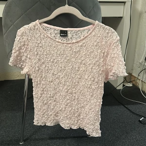 Ljusrosa spetsig topp från Gina Tricot - Säljer en ljusrosa topp från Gina Tricot med korta ärmar och spetsigt, strukturerat material. Toppen har rund halsringning och är perfekt för att ge en söt touch till din outfit.