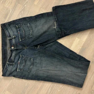 Blå jeansbyxor från Maingott lågmidjade  - Mörkblå jeansbyxor från Maingott med klassiska fem fickor och kontrastsömmar. Byxorna har raka ben/ utsvängda ben och normal passform, samt detaljer med röda sömmar på fickorna. . Passar xs-s