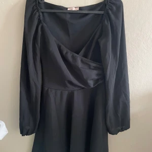 Svart omlottklänning med lång ärm - Säljer en svart klänning med omlott-detalj framtill och långa ärmar. Klänningen har en djup v-ringning och lätt utställd kjol. Perfekt för dig som gillar stilrena och klassiska plagg. Använd 2ggr.