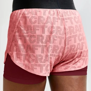 Rosa träningsshorts från Craft - Snygga rosa träningsshorts från Craft med perforerat mönster och dubbla lager. Yttershortsen är ljusrosa med logotypmönster, och innershortsen är mörkröda. Perfekta för löpning eller gym.