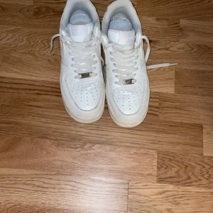 Vita Nike Air Force 1 sneakers - Klassiska helvita Nike Air Force 1 sneakers med snörning och rund tå. Skorna har en platt sula och är tillverkade i syntetmaterial med diskret Nike-logga på sidan. Perfekta för en clean och stilren look. Använda 5 gånger och lite creasadew