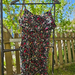 Svart blommig kortklänning med smala axelband - Säljer en svart kortklänning med färgglatt blommönster och smala axelband. Klänningen har en figurnära passform och är perfekt för varma dagar. Lätt och luftig känsla, passar dig som gillar romantisk stil.