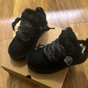 Svarta skor från uggs - Snygga svarta sneakers från UGG med tjocka snören och pälsdetaljer. Skorna har en robust sula och är fodrade för extra värme. Perfekta för kyligare dagar.