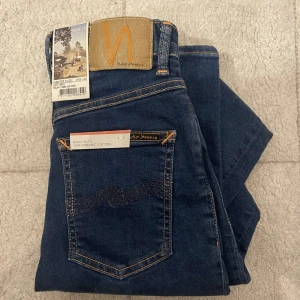 Nudie jeans (helt NYA) - Snygga mörkblå jeans från Nudie Jeans med klassisk femficksdesign och kontrastsömmar. Tillverkade av 100% ekologisk bomull. Märkespatch i läder baktill och diskret broderad bakficka.