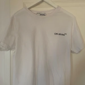 Vit t-shirt från Off-White med tryck - Vit t-shirt från Off-White med svart logga på bröstet och stort färgglatt tryck på ryggen med sneakers och Off-White detaljer. Klassisk rund hals och korta ärmar. Perfekt för dig som gillar streetwear och snygga prints.