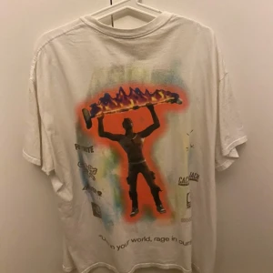 Vit Cactus Jack x Fortnite t-shirt - Vit t-shirt från Cactus Jack x Fortnite med tryck av en figur som håller upp ett brinnande skateboardliknande objekt på ryggen. Framsidan har en liten text på bröstet. T-shirten är i bomull och har normal passform och korta ärmar.