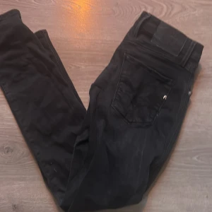 Svarta jeansbyxor från Replay Anbass - Säljer ett par svarta Replay Anbass jeans med klassisk femficksdesign och dragkedja. Byxorna har en slim passform och är tillverkade i ett stretchigt material som sitter snyggt. Perfekta för dig som gillar stilrena och bekväma jeans.