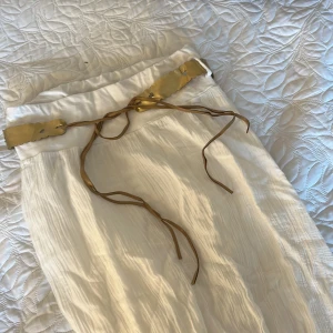 Vit långkjol med guldfärgat bälte - Säljer en vit långkjol och ett  guldfärgat bälte med bruna band. Bältet går och ta av. Kjolen har en luftig och perfekt för varma dagar. Skriv för ändringar inom priset!💗