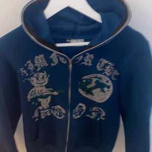 Blå hoodie med glittrigt tryck - Säljer en blå hoodie från aim for the moon med glittrigt tryck framtill och dragkedja. Tröjan har huva och långa ärmar, perfekt för en cool och avslappnad stil.
