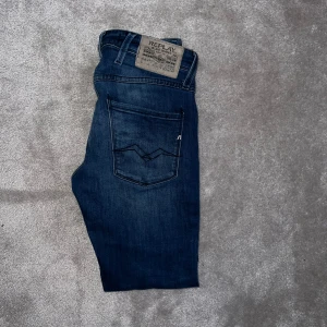 Replay Anbass Jeans - Säljer ett par medium blå jeans från Replay med klassisk femficksdesign och snygga detaljer på bakfickorna. Width: 28 Length: 30. Jeansen är slim fit. Använd fåtal gånger och köpta på NK. Hör av dig vid fundering!