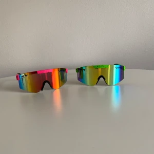 Pitvipers solglasögon - Två par spegelglasade solglasögon med sportig look och stora, rektangulära linser. Ena paret har rosa och orange detaljer, det andra gröna och blå. Perfekta för en färgstark stil och aktiva dagar. Skriv för pris för en eller andra funderingar.
