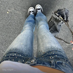 Blå bootcut jeans med strassdetaljer - Säljer ett par blå bootcut jeans med låg midja och snygga strassdetaljer framtill. Jeansen har en klassisk femficksmodell och är i ett tvättat denimtyg. Perfekta för dig som vill sticka ut lite extra med glittriga detaljer.