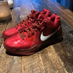 Kd 3 allstar - Säljer ett par röda Nike basketskor med vit swoosh på sidan. Skorna har snörning och en platt sula med mönstrad undersida för bra grepp. De har en sportig look och är tillverkade i syntetmaterial.