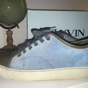 Blå Lanvin Captoe - Snygga blå sneakers från Lanvin med ovandel i mocka och detaljer i grått skinn. Skorna har snörning och vit platt sula, perfekt för en stilren och avslappnad look. Låda medföljer, lätt och restorera för den som har tid. pris är alltid diskuterbart. Storlek uk7