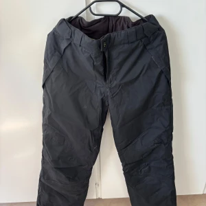 Svarta täckbyxor från H&M Sport - Svarta täckbyxor från H&M Sport med dragkedja och knapp framtill. Byxorna har en sportig look och är fodrade med limegrönt innerfoder. Perfekta för vinterns utomhusaktiviteter.