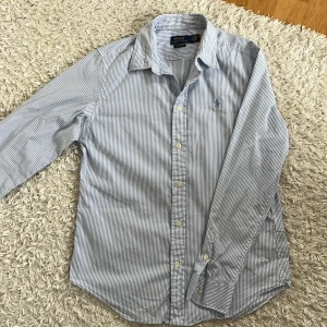 Blårandig skjorta från Polo Ralph Lauren - Säljer en klassisk blårandig skjorta från Polo Ralph Lauren med broderad logga på bröstet. Storleken är 8 som jag skulle säga motsvara S herr och skjortan är i classic fit. Skjortan är i ett mjukt bomullsmaterial. Perfekt för en stilren look!