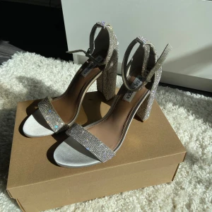 Klackskor med strass (stenar) från Steve Madden - Säljer dessa klackskor från Steve Madden i silver/strass stenar med satin ”detaljer”. Aldrig använda! Nypris 1300kr. Storlek 40, men de är som storlek 38/39. Klackhöjd 10 cm. Perfekta skor till bal/student💗. 750kr
