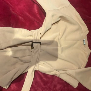 Rosa tröja med bälte - Säljer en rosa tröja med lång ärm och matchande bälte i midjan. Tröjan har en enkel, rak design och är tillverkad i ett mjukt tyg som ger en avslappnad men stilren look. Perfekt för dig som gillar minimalistisk stil.