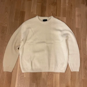 Beige stickad tröja med rund hals - Säljer en enkel och stilren vit stickad tröja med rund halsringning. Tröjan har långa ärmar och ribbade muddar vid ärmslut och nederkant. Oversized