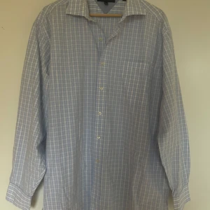 Blårutig skjorta från Tommy Hilfiger - Klassisk blårutig skjorta från Tommy Hilfiger med lång ärm och knappar framtill. Skjortan har en mjuk krage och diskret bröstficka. Perfekt för en stilren och avslappnad look.