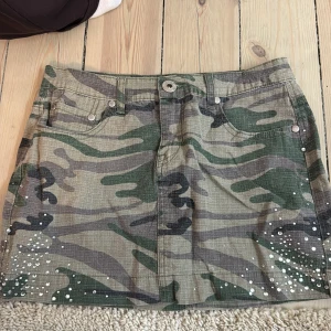 Camo minikjol med pärldetaljer - Cool camouflagemönstrad minikjol med vita pärlor längs nederkanten och bakfickorna. Kjolen har klassisk jeansmodell med fickor fram och bak 💕💕💕💞