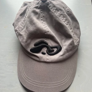 Keps Weekday - Säljer en keps från Weekday i bomull med justerbart spänne bak. Kepsen har ett svart broderat motiv framtill och klassisk böjd skärm. Använd en gång🩶